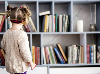 a little girl chooses a book in her home library