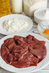 Raw liver on a white plate on a wooden background. A set of products for cooking fried liver egg oil salt flour. Food ingredient. Selective focus.