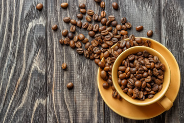 A coffee cup with coffee beans on an old wooden table. Fried coffee beans on a wooden background. Viewing from above.