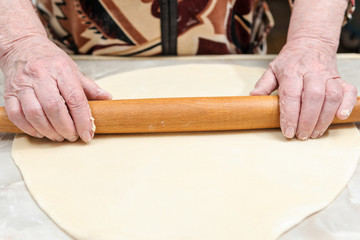 Hands of the old woman roll the dough on the table