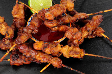 Sticky chicken skewers with chilli sauce dip on a slate stone background