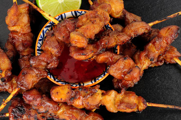 Sticky chicken skewers with chilli sauce dip on a slate stone background