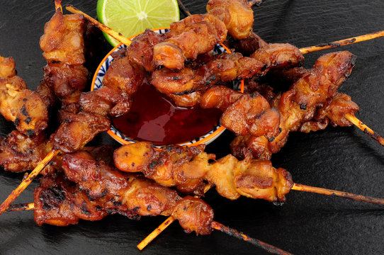 Sticky chicken skewers with chilli sauce dip on a slate stone background