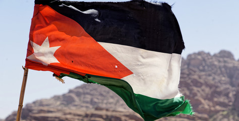 Slightly battered flag of the land Jordan on the high windy cliffs of Petra, Wadi Musa, Jordan,