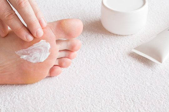 Groomed man's hands applying feet moisturizing cream. Bare feet on the white towel. Cares about clean and soft legs skin. Healthcare concept.