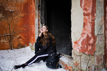 Fashionable long legs brunette model in long black cloak posed outdoor at winter day against old grunge wall.