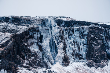 Fototapeta premium Dramatic icelandic landscape with snow covered mountains with frozen warefall.