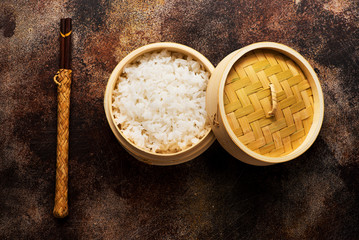 Rice in bamboo steamer with chopsticks on a brown concrete background, top view