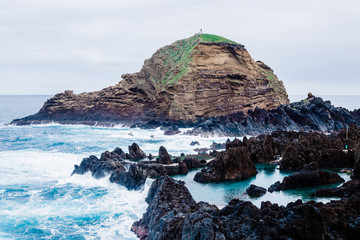 Natural swimming pools, rocky shore and blue ocean waves during cloudy day in Porto Moniz, Madeira, Portugal