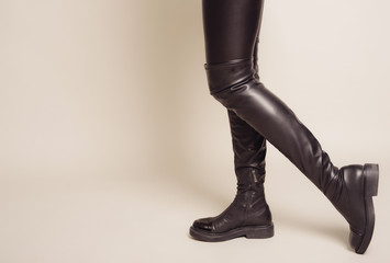 Slim women's legs in black leather pants and stylish high boots stands sideways