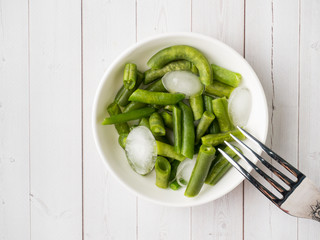 Green beans pod with ice pieces on a white plate