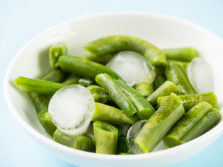 Green beans pod with ice pieces on a white plate