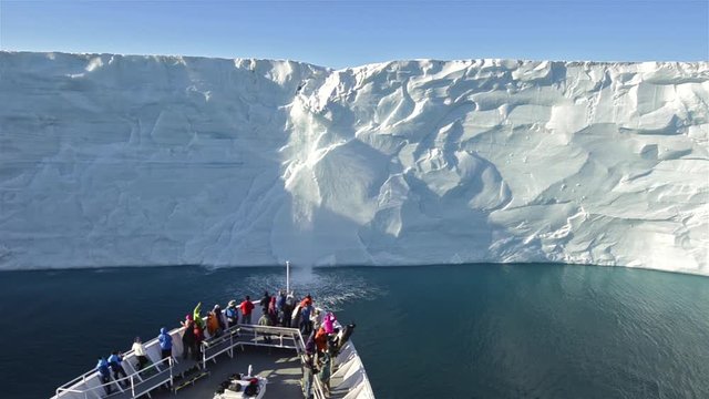 A waterfall flows off the Austfonna icecap in Norway suggesting global warming with ship foreground.
