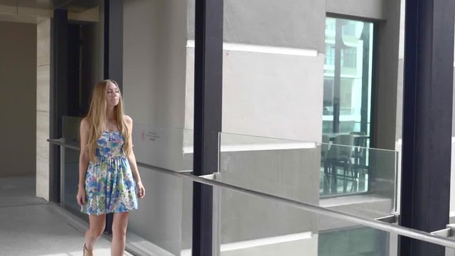 Young attractive woman in colorful summer dress walking along hte hall in business center.