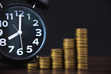 Alarm clock and step of coins stacks on working table in dark room, time for savings money concept, banking and business concept.