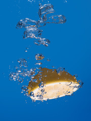 Half lemon splashing in the water with a couple of air bubbles.