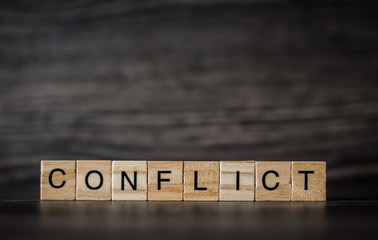 the word conflict, consisting of light wooden square panels on a dark wooden background