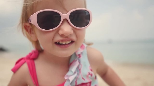 A little sweet girl in a choca in polka dots, standing on the beach of children's sunglasses. slow motion. 1920x1080. full hd
