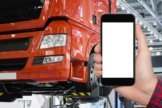 Hand with phone on a background of truck on a lift in a car service