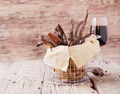 jerked meat, cow, deer, wild beast or biltong with wine bowls on a rustic table, selective focus