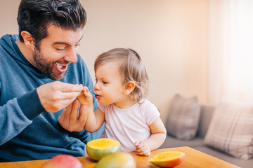 Father feeding toddler baby infant with spoon and mango