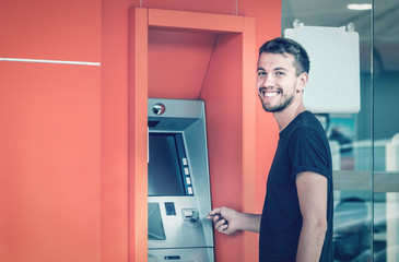 Young smiling man using ATM machine