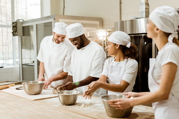 group of happy multiethnic bakers kneading dough together - obrazy, fototapety, plakaty