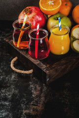 Fresh fruit and juices variety. Oranges, pomegranate and apples. Dark rusty background, with wooden tray, copy space