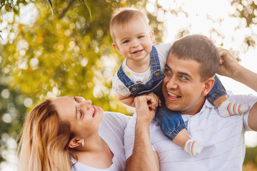 Dad holds little daughter on his neck standing with a mom in the park
