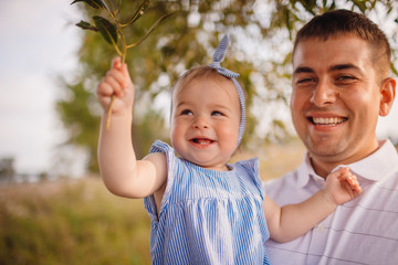 Happy father holds charming little girl standing in the garden