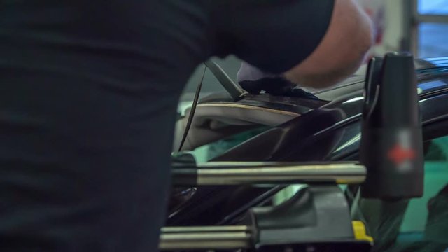 A mechanic is taking down a black rubber that was on the front window of a car. He needs to replace this window.