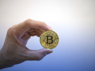 Bitcoin in gold color held by hand on white background and gradient blue