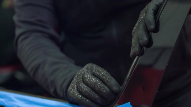 A mechanic is fixing a car window in an automobile repair shop. He is wearing safety gloves.