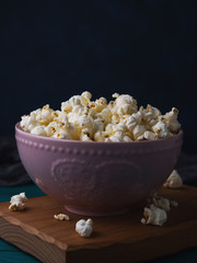 Popcorn in pink bowl on wooden board on dark background