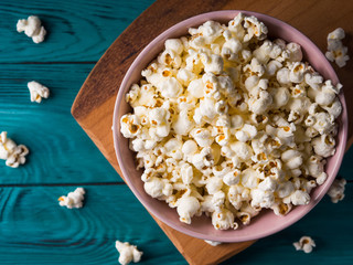 Popcorn in pink bowl on wooden board on dark green background
