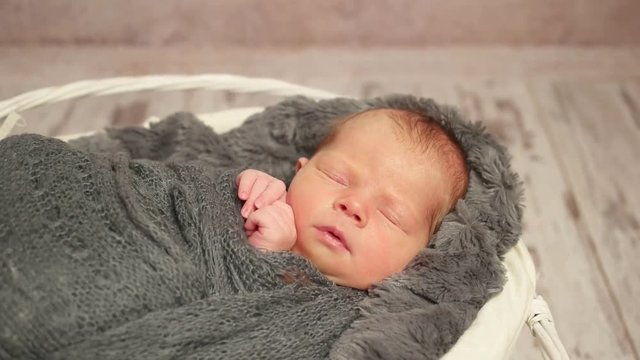 Small child napping in his basket with tiny hands pressed to his cheek, wrapped up