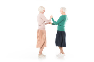 Side view of two senior stylish women holding hands of each other isolated on white