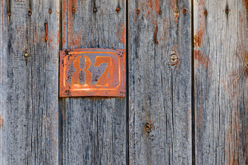 Rusty metal house number plaque No. 87 on an old wooden door
