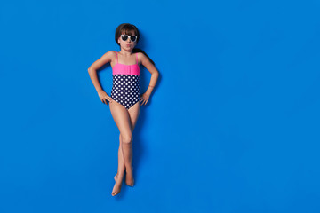 Child bikini view top.Little stylish lady girl in swimsuit,relaxing isolated blue background.Lovely photo for advertising,copy space for text.Beach Vacation concept.Kid model lay full-length.