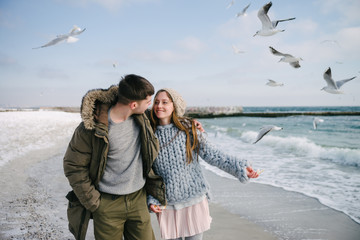 happy couple hugging and walking on winter sea shore with seagulls