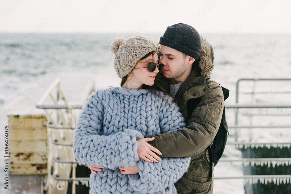 Wall mural young boyfriend hugging his stylish girlfriend in merino sweater on winter quay