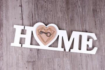 The key in the heart on the word Home in front of wooden background