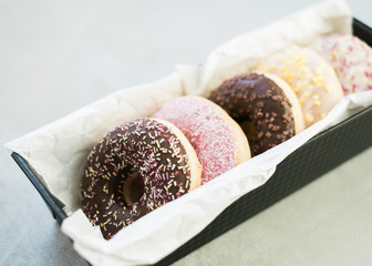 Close-up of a metal Tin on a table filled with assorted donuts with frosting and sprinkles