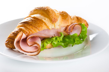 Fresh croissant with ham and salad leaf on white