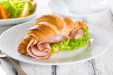 Fresh croissant with ham and salad leaf with sfresh salad on white wooden background