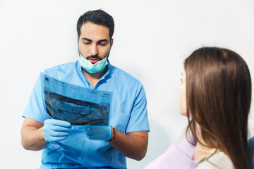 Fototapeta na wymiar Dentist using x-ray during dental treatment, pointing at the teeth scan and explaining the problem, pretty woman in white top sitting in dental chair at the doctor's