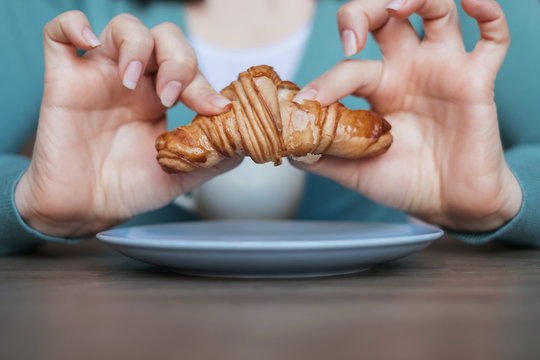 Close-up of a woman sitting at a table holding a croissant with both hands