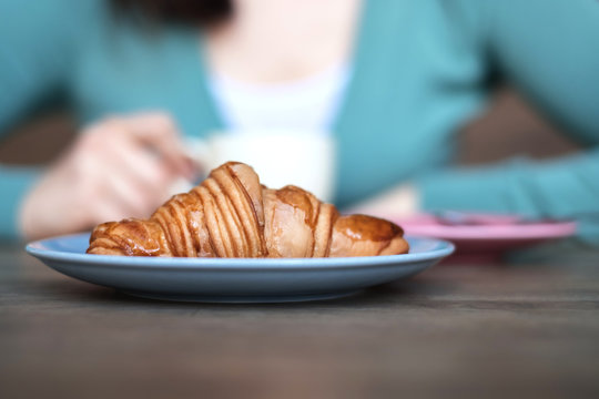 Croissant in front of a woman drinking coffee