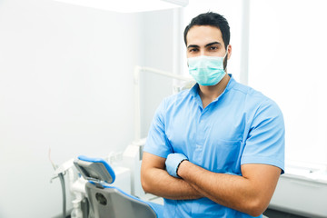 Fototapeta na wymiar Portrait of hadsome dentist doctor wears blue uniform and face mask, indoor shot in modern dentist office