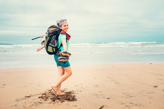 Happy girl backpacker traveler runs barefoot on the sand ocean beach